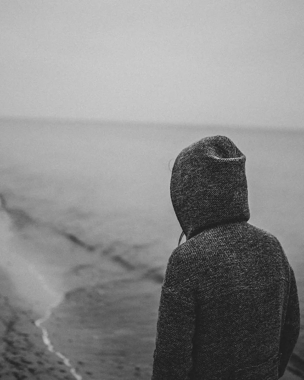 Pessoa de moletom com capuz olhando o mar