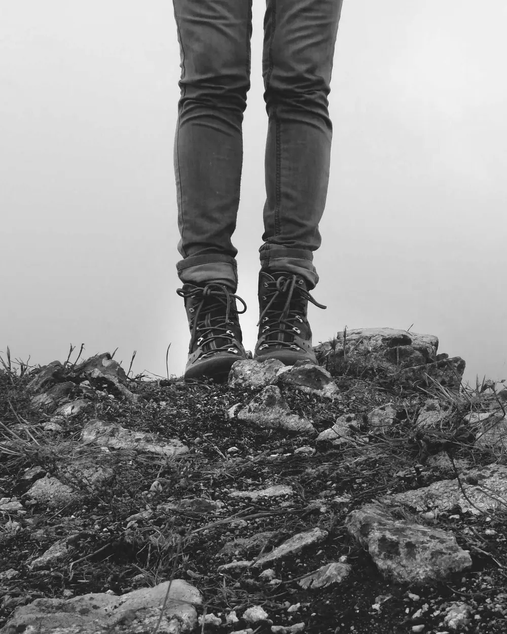 Detalhe de calça e botas sobre pedras, com neblina ao fundo
