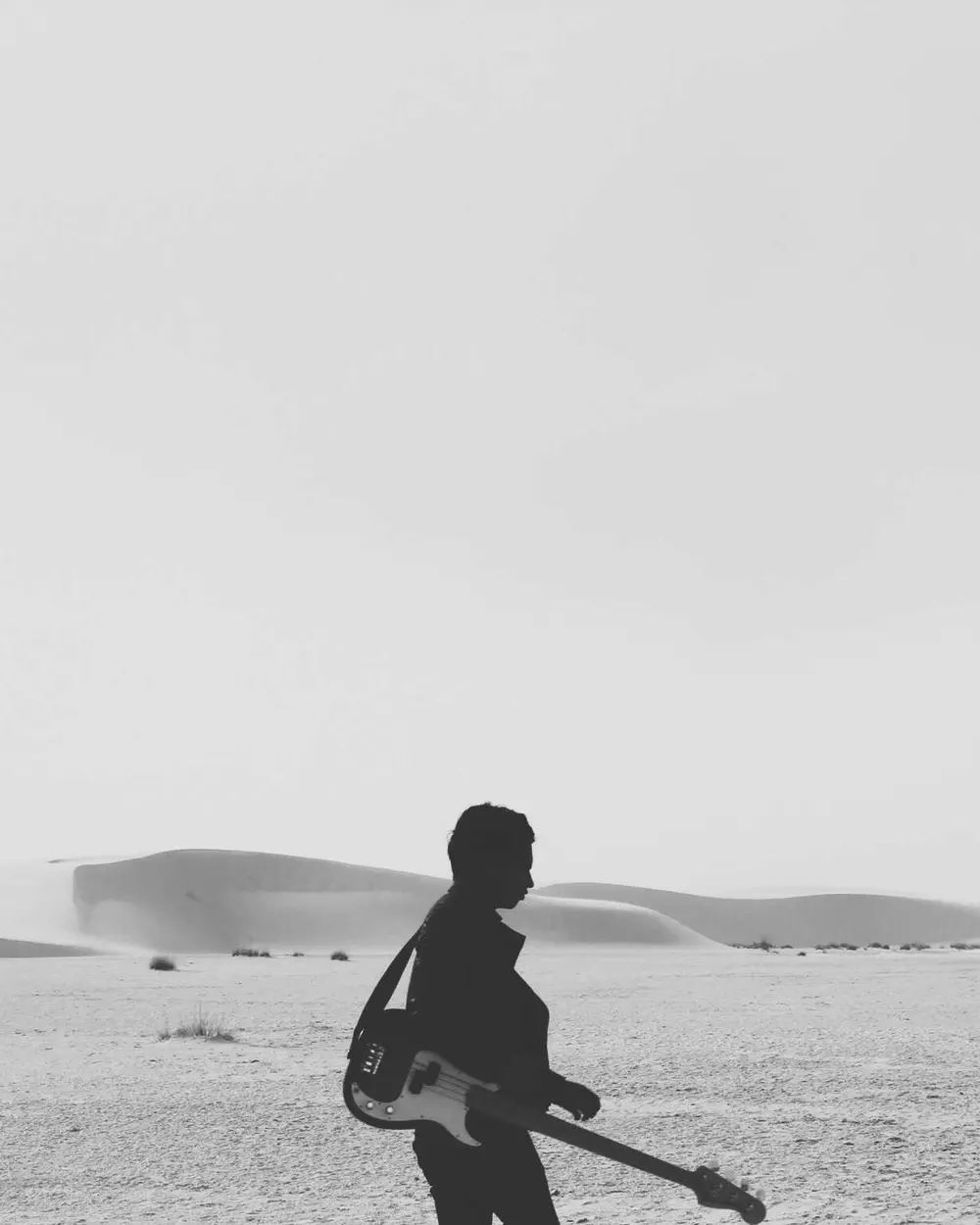 Pessoa com guitarra caminhando em uma paisagem de dunas